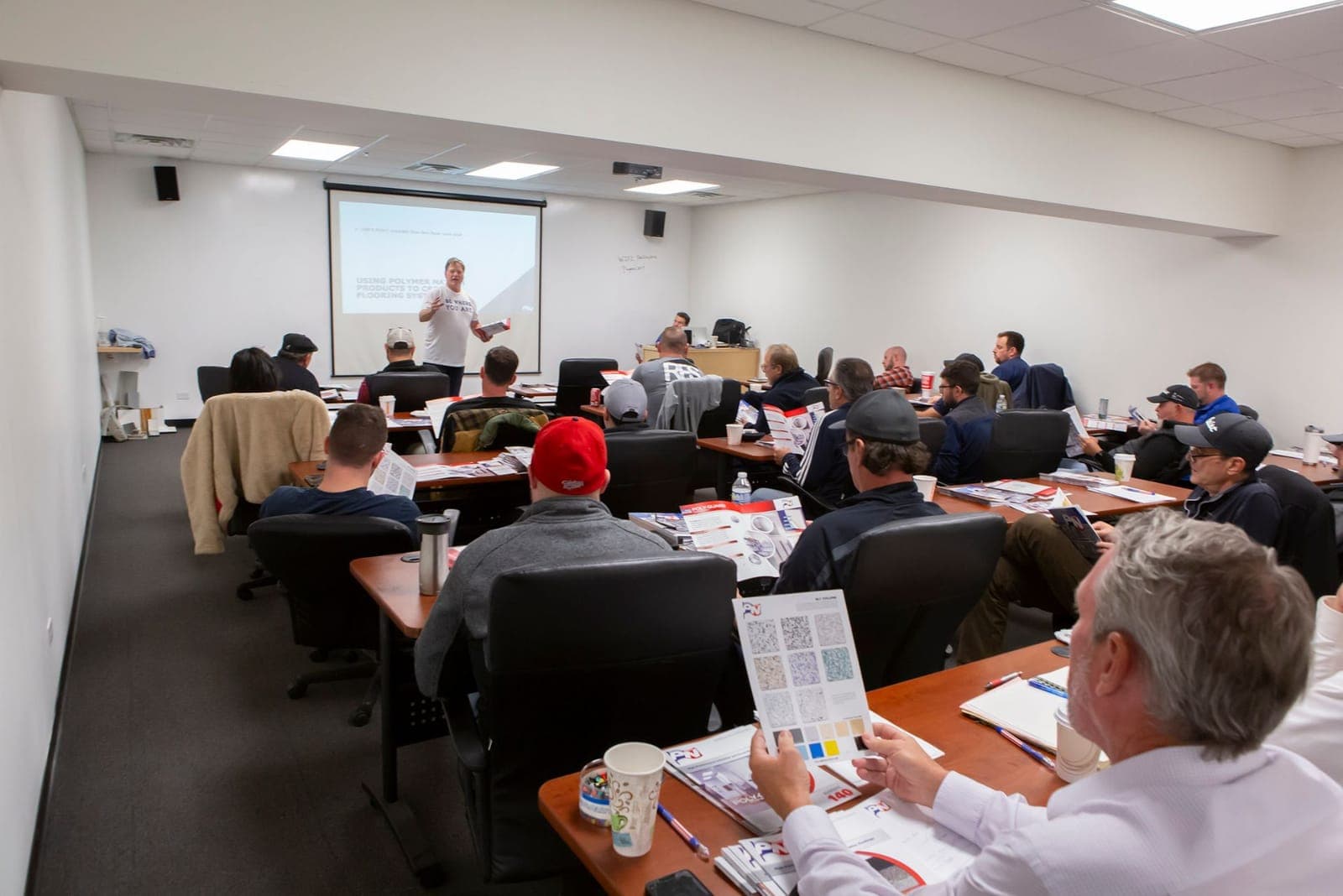 Classroom session in progress — attendees at tables reviewing Polymer Nation system and color literature while an instructor presents